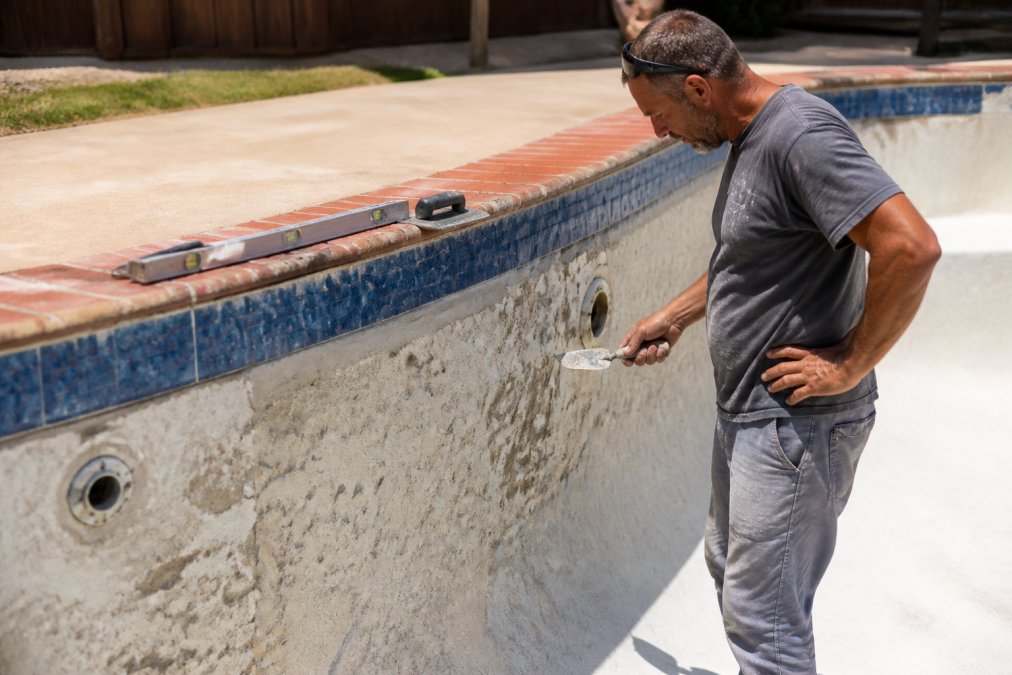 Pool technician inspecting a cracked surface during pool plaster repair in an empty residential pool