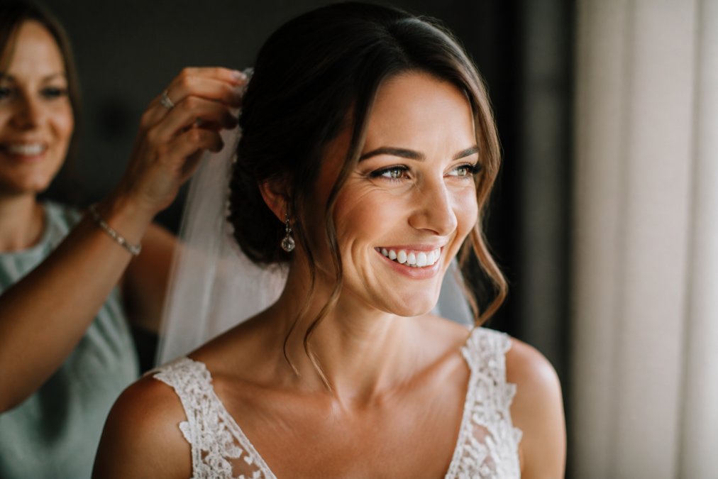 Bride smiling confidently during wedding day with close-up of natural-looking porcelain veneers catching soft natural light, radiant expression in bridal gown