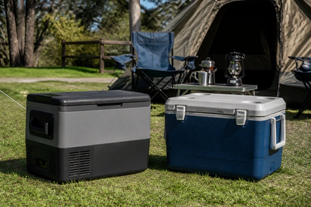 A portable compressor fridge and traditional esky cooler positioned side by side at a campsite with a tent and camping setup visible in the background during daytime