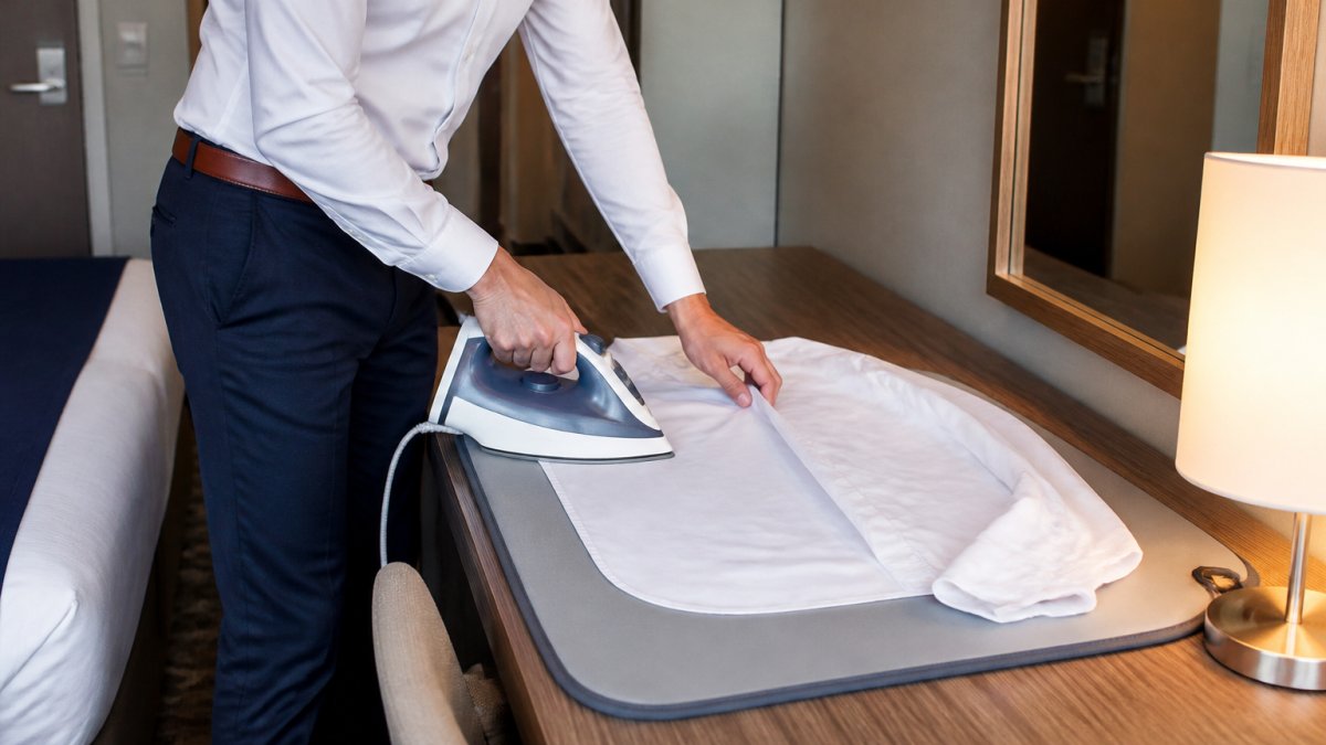 Professional demonstrating portable ironing mat setup on hotel room desk with iron positioned on heat-resistant surface, showing proper technique in compact hotel environment