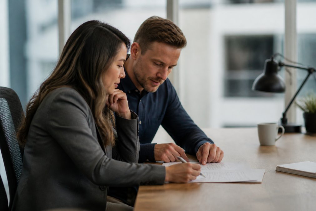 Two accounting professionals sitting side by side at a workstation, reviewing property management software on dual screens in a modern office