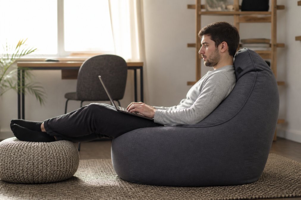 Person working from home in ergonomic beanbag setup, demonstrating proper spinal alignment and relaxed posture with good neck support during extended work session in bright home office