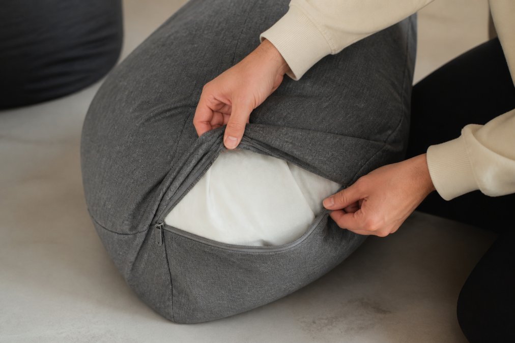 Close-up of hands carefully removing a removable fabric cover from a pouf, revealing the inner structure, demonstrating the ease and practicality of maintenance