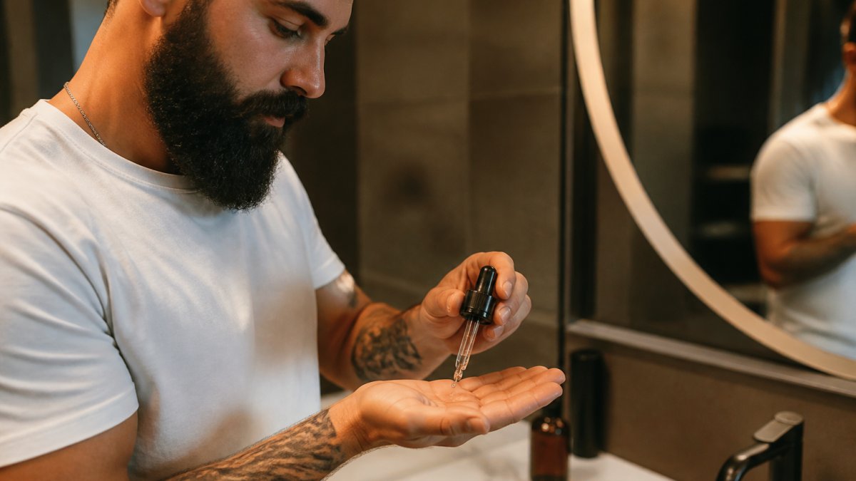 Un homme applique quelques gouttes d'huile pour son soin de barbe dans une salle de bain moderne.
