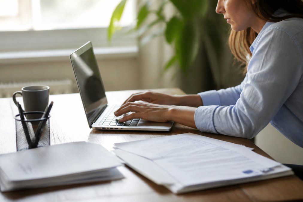 Persona usando un ordenador portátil en un escritorio moderno para rellenar un formulario de presupuesto online, con documentos digitales visibles en pantalla y luz natural de fondo