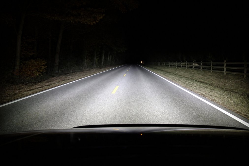 Nighttime road scene showing vehicle headlights illuminating the pavement and lane markings, demonstrating beam cutoff pattern and road visibility