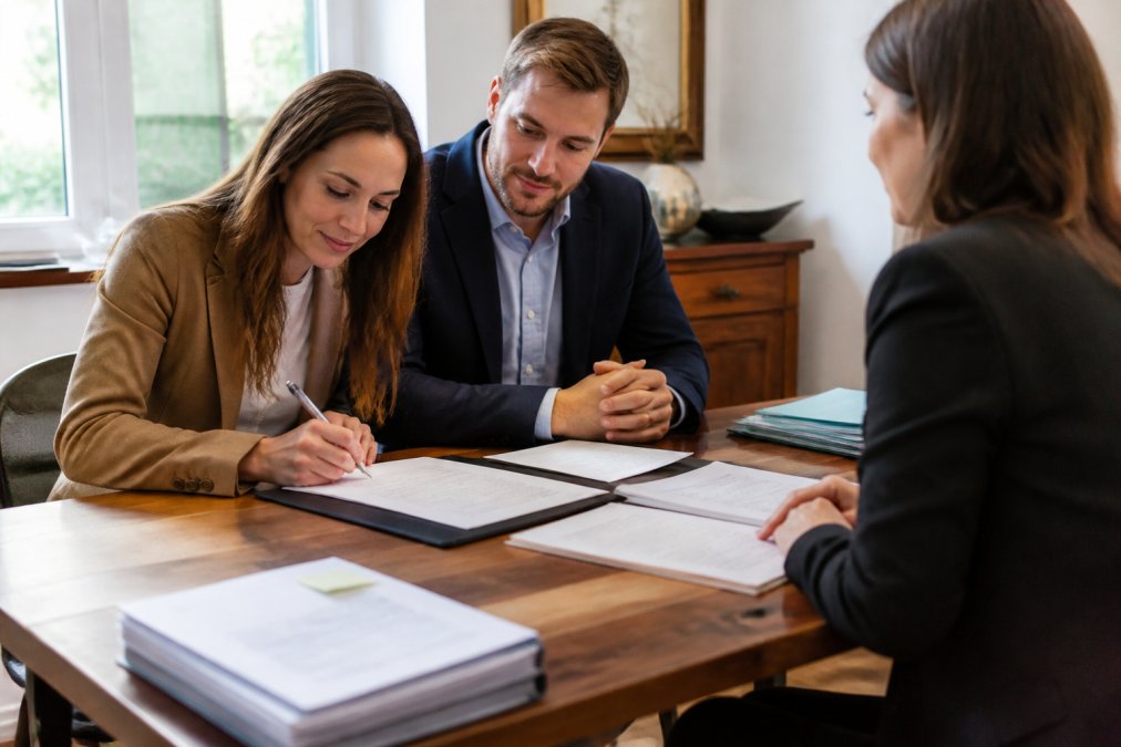 Un couple signe les documents officiels de son premier achat immobilier lors d'un rendez-vous chez le notaire avec des actes.