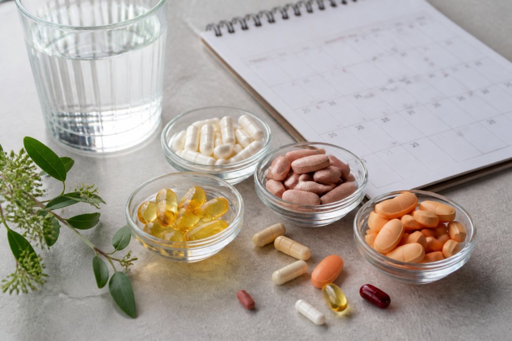 Assorted bariatric vitamin capsules and chewable tablets arranged on a light background with a calendar and water glass