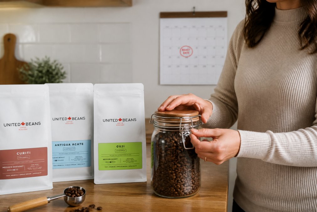 Hands carefully sealing an airtight glass storage container filled with freshly roasted whole coffee beans in a bright home kitchen, with a calendar visible on the wall showing the roast date