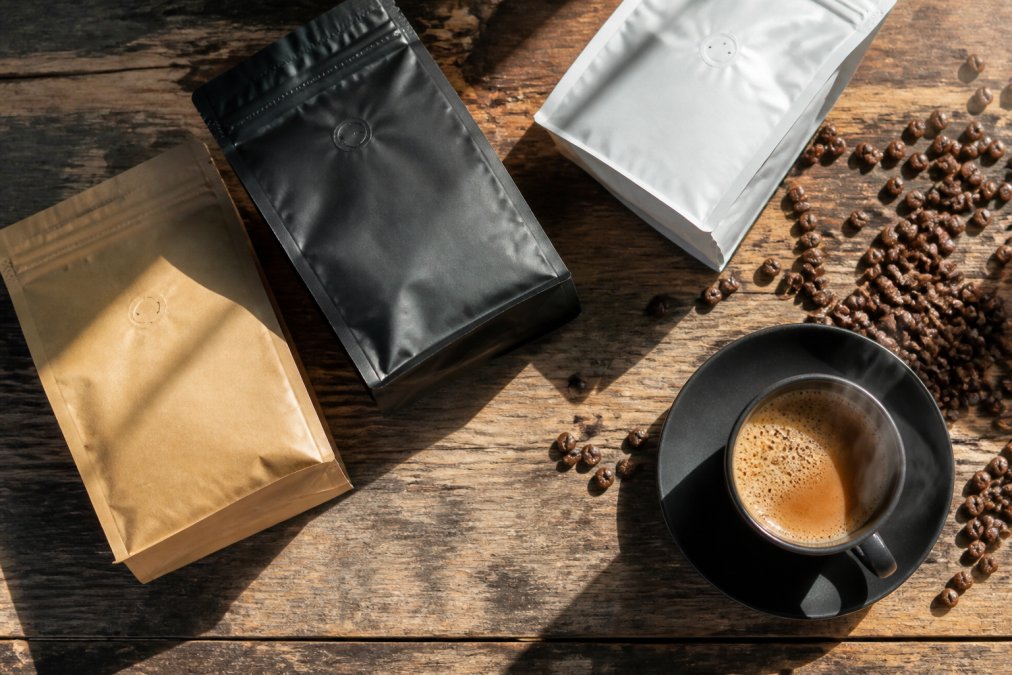 Overhead flat lay of multiple Iron Spur Coffee bags arranged on weathered wood surface with steaming cup of brewed coffee, whole beans scattered nearby, and morning light streaming across the scene