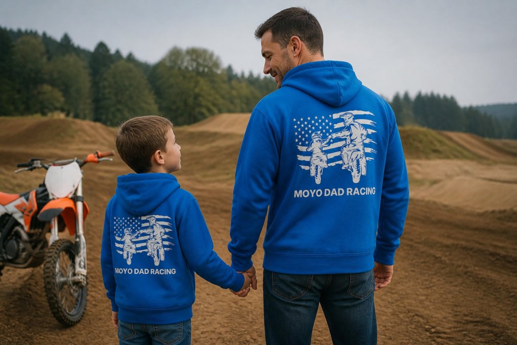 Father and son wearing matching motocross-themed hoodies standing together at a dirt bike track or practice area