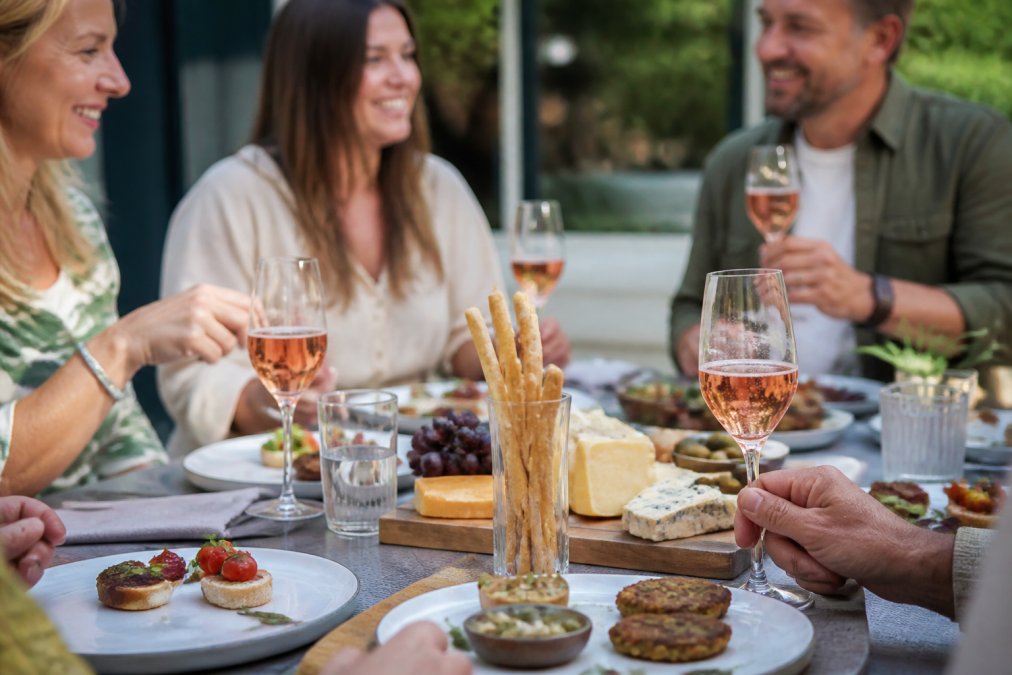 A table setting with a glass of alcohol-free sparkling rosé, a cheese board and small plates of canapés, natural daylight, relaxed dinner party scene