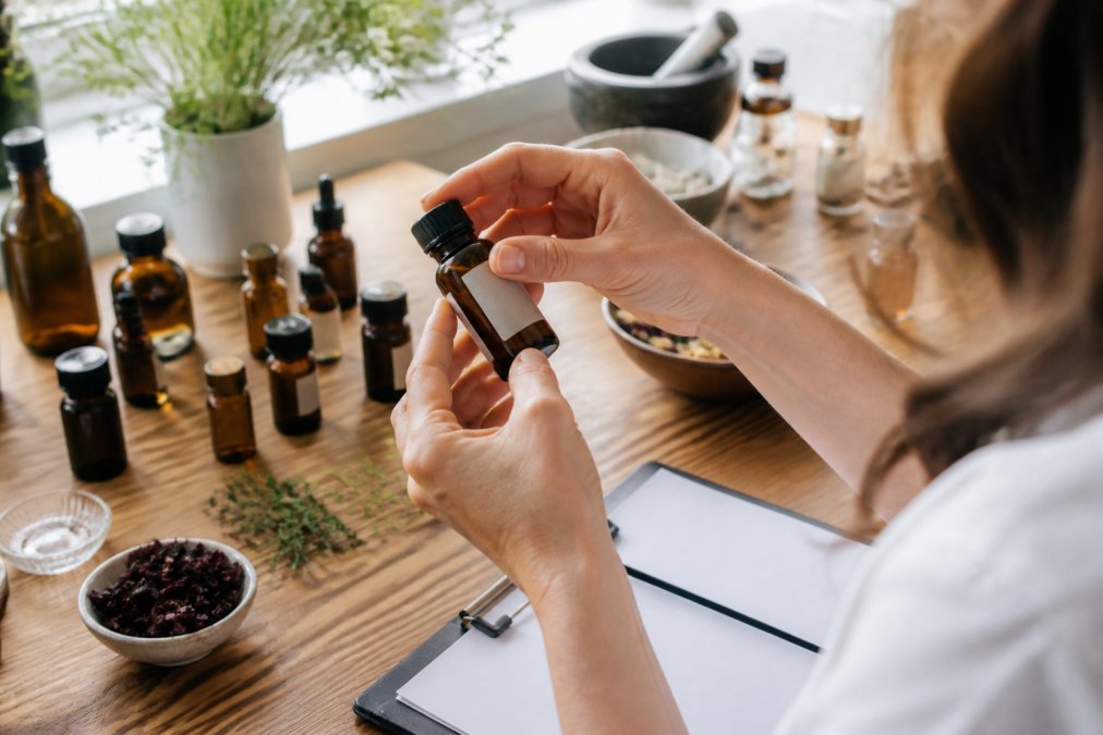 Close-up of hands examining amber glass essential oil bottles, checking labels for GC/MS testing information and botanical extraction methods under natural light