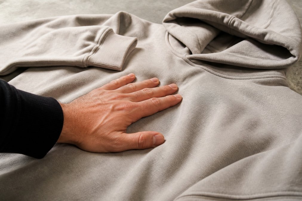 Close-up of a person running their hand over a thick, structured 300GSM cotton oversized hoodie laid flat on a clean surface, showing the weight and texture of the fabric
