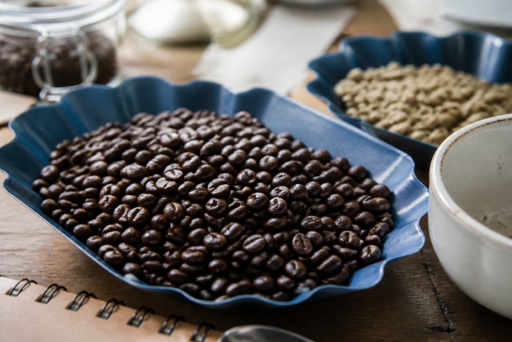 Close-up of freshly roasted specialty-grade Arabica beans with visible oil sheen and rich brown color variation, roast date label visible on the side, natural morning light highlighting the bean surface