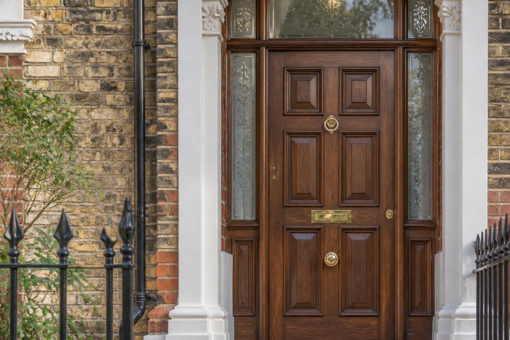 Close-up of an elegant timber entrance door featuring brass hardware, Georgian-style detailing, and intricate panelling on a Victorian terrace property with period brickwork visible