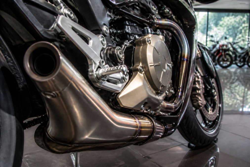 Close-up van een gepolijste titanium uitlaat en motorblok van een exclusieve sportmotor in een toonzaal, met reflecterend licht op het metaal