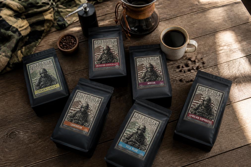 Overhead flat-lay of multiple coffee bags with military-inspired vintage packaging arranged on a wooden surface with a filled ceramic mug and brewing equipment nearby, natural daylight streaming across the scene
