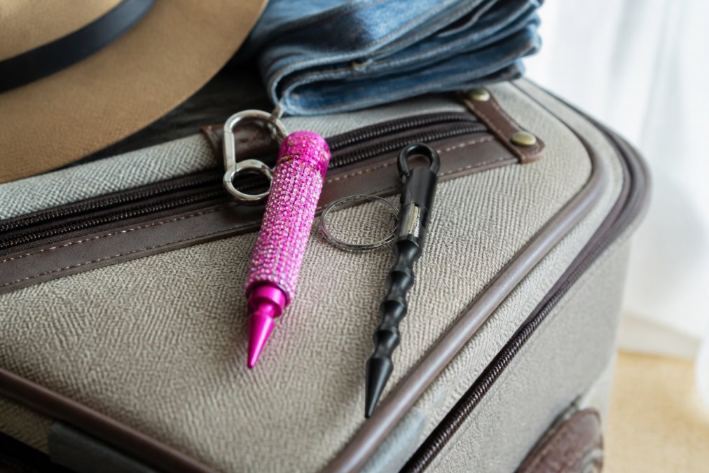 Close-up of a stylish rhinestone-embellished self-defense keychain next to a minimalist functional keychain on a traveler's packed bag, showing contrast in design and materials, natural daylight
