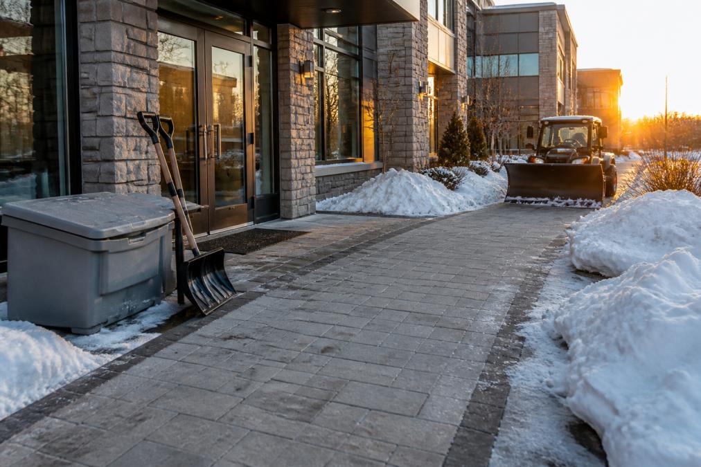 Cleared stone walkway at a commercial building with salt bins and snow removal equipment to prepare commercial grounds