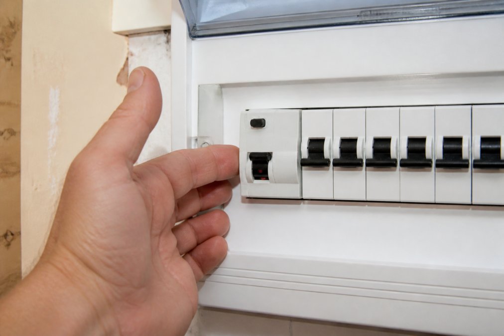 Close-up of a hand positioned near a switchboard showing the main safety switch lever in the tripped position, with clear visibility of the reset mechanism and surrounding circuit breakers