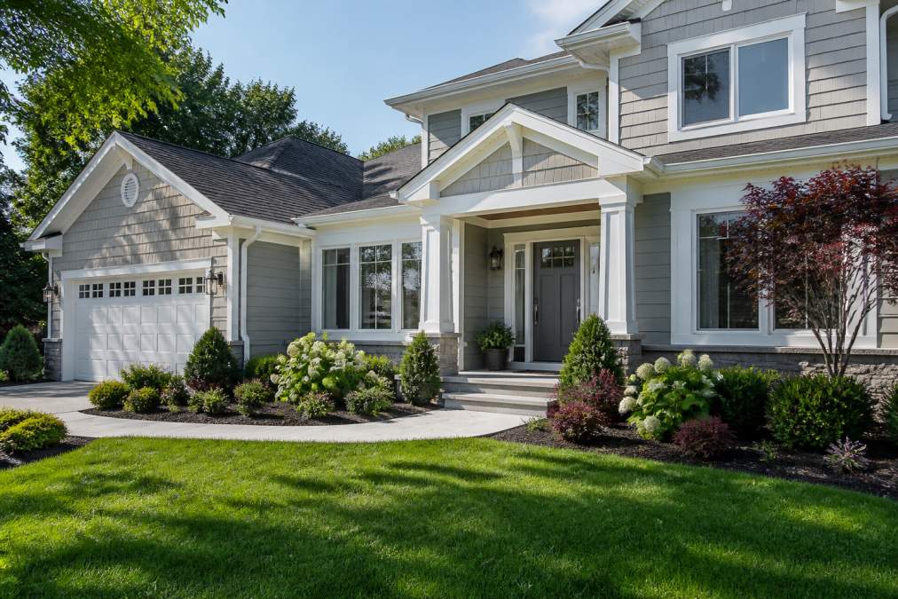 A well-maintained home exterior with freshly cleaned siding, manicured landscaping, vibrant green lawn, and a welcoming front entrance painted in neutral tones on a bright sunny morning