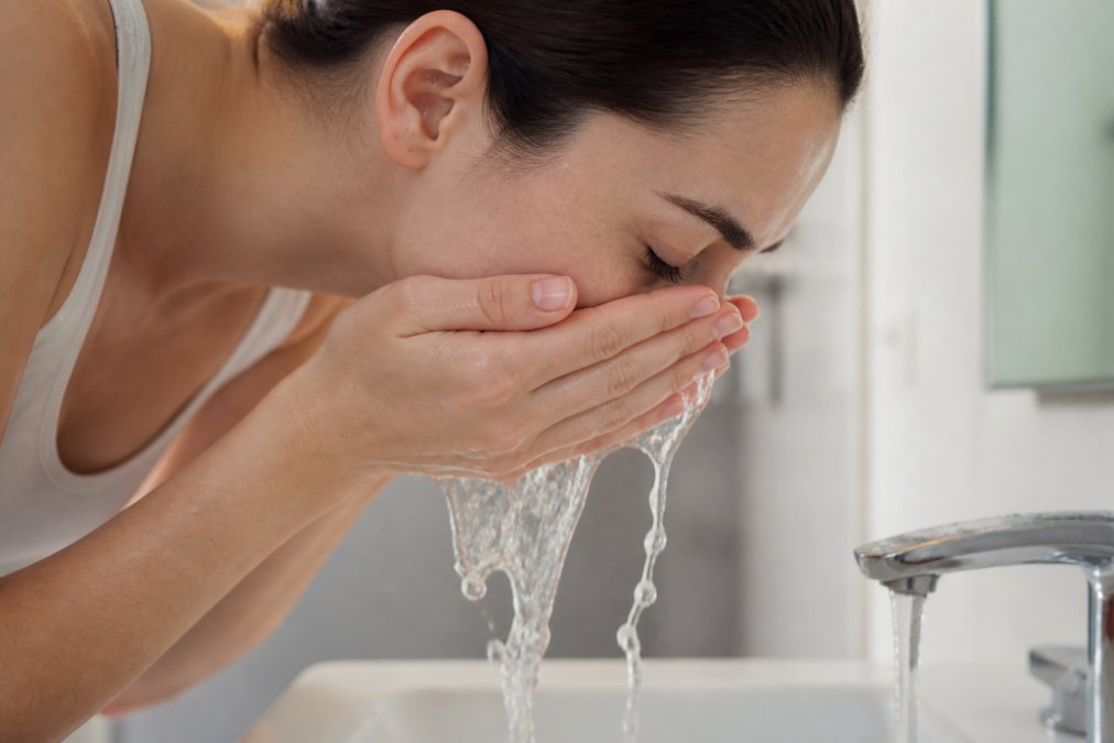 Close-up of hands gently washing face with water running over fingertips, showing proper cleansing technique with soft contact on skin surface