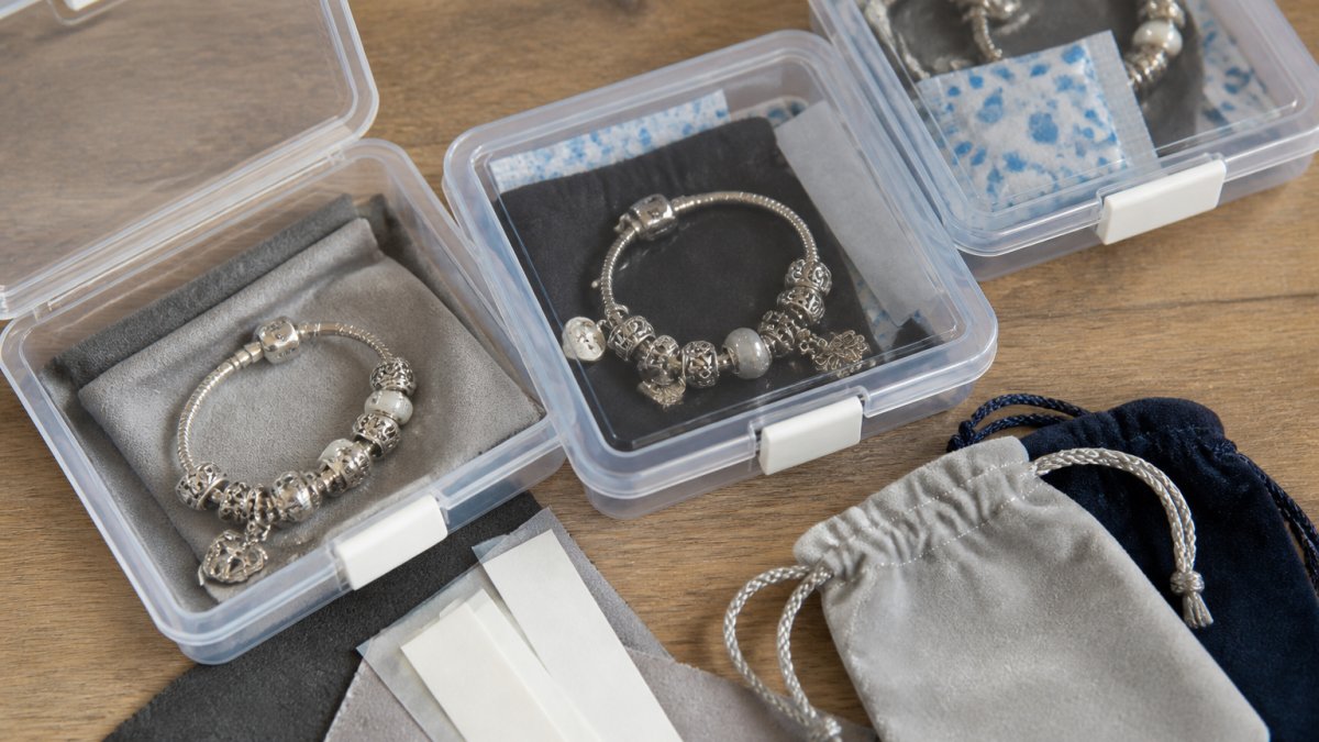 Close-up of organized sterling silver charm bracelets stored in airtight containers with silica gel packets, anti-tarnish strips, and soft pouches visible inside