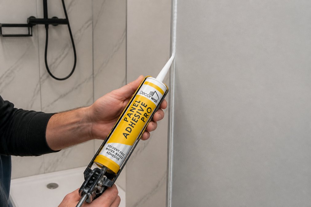 Professional hands applying silicone sealant along the edge of bathroom wall panels during installation, showing proper sealing technique with smooth, continuous bead and caulking gun