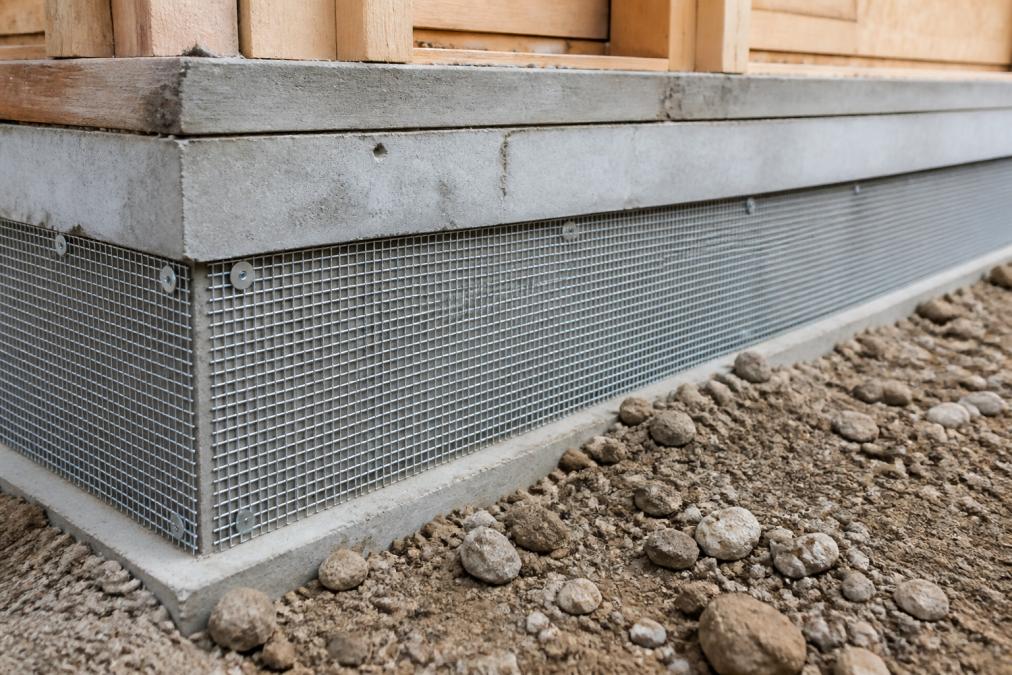 Close-up of sealed concrete barrier with metal mesh screening installed on building foundation, showing proper installation technique with minimal gaps