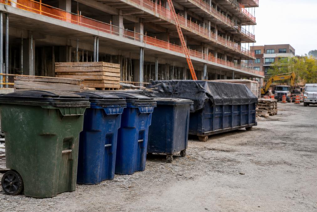 Construction site showing organized waste bins with tight-fitting lids, covered dumpsters, and cleared debris removal area with clean ground surface