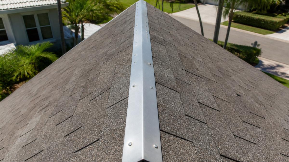 Close-up of a roof ridge showing zinc strips installed along the peak with clean asphalt shingles visible in daylight