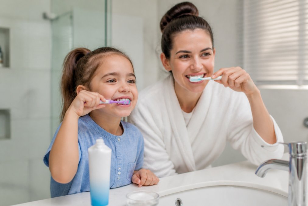 Parent and child brushing teeth together as part of preventative dental care in a bright bathroom