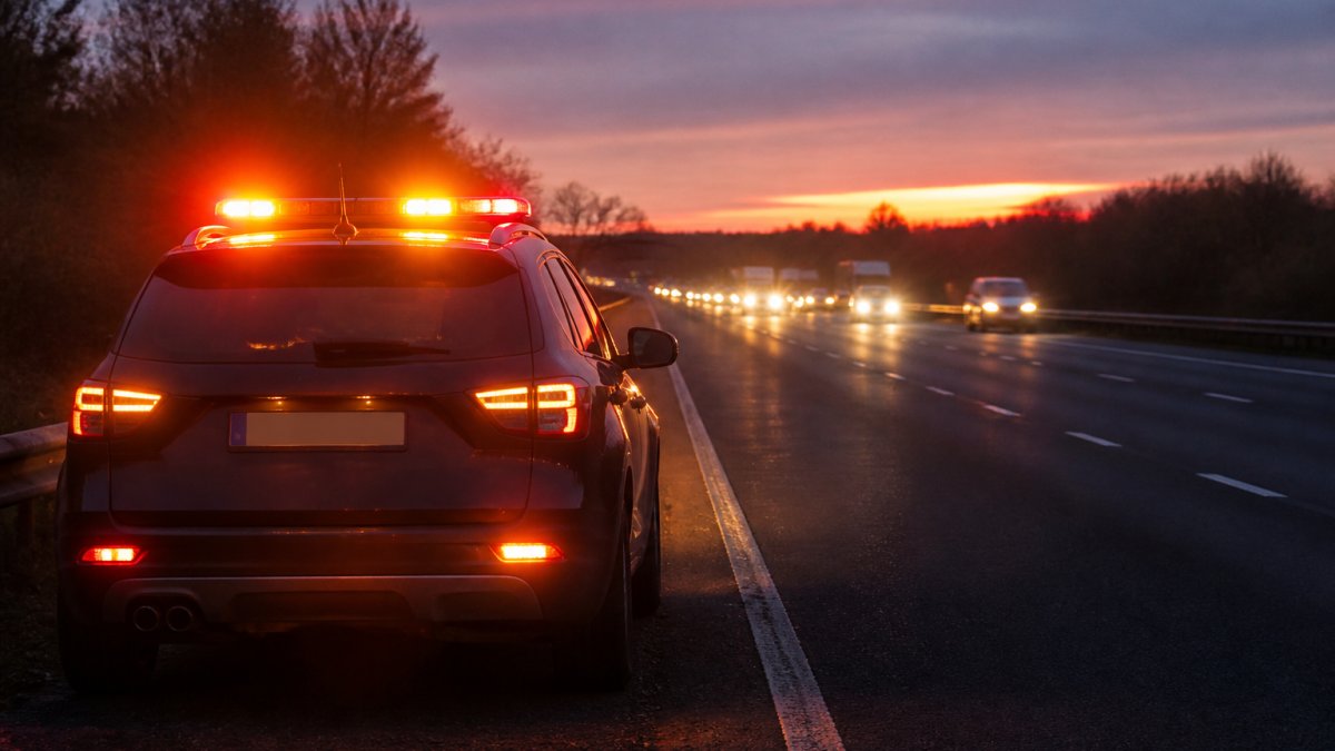 Preventing Glare from Vehicle Warning Lights Stationary vehicle on motorway at dusk with amber and red warning beacons properly positioned on roof and rear, hazard lights flashing, with approaching traffic visible in distance under twilight sky