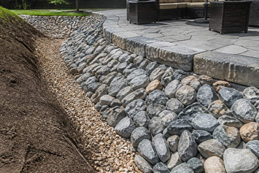 Professionally installed riprap and stone barriers protecting a patio edge, showing properly sized stones, compacted soil foundation, and water drainage channels