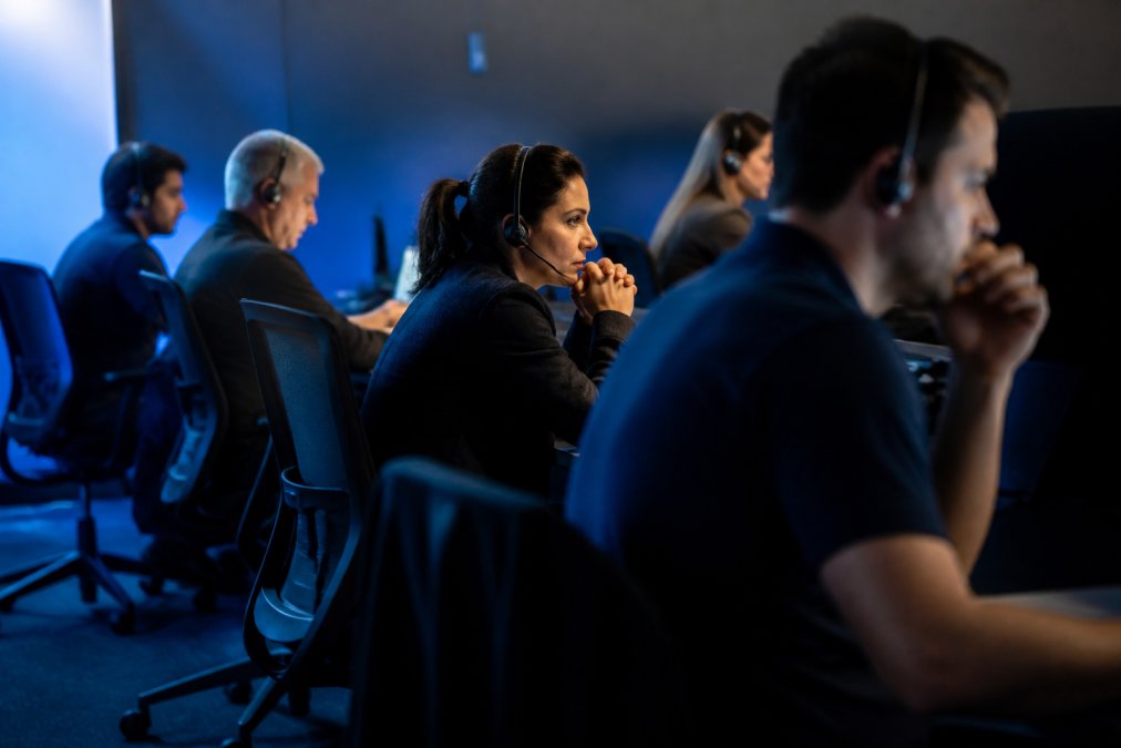 Cybersecurity team monitoring multiple screens displaying real-time threat alerts and system logs in a secure operations center with dim blue lighting and rows of workstations