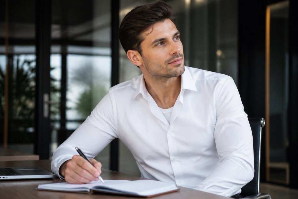 Professional sitting at an office desk wearing a crisp white dress shirt with a visible undershirt neckline