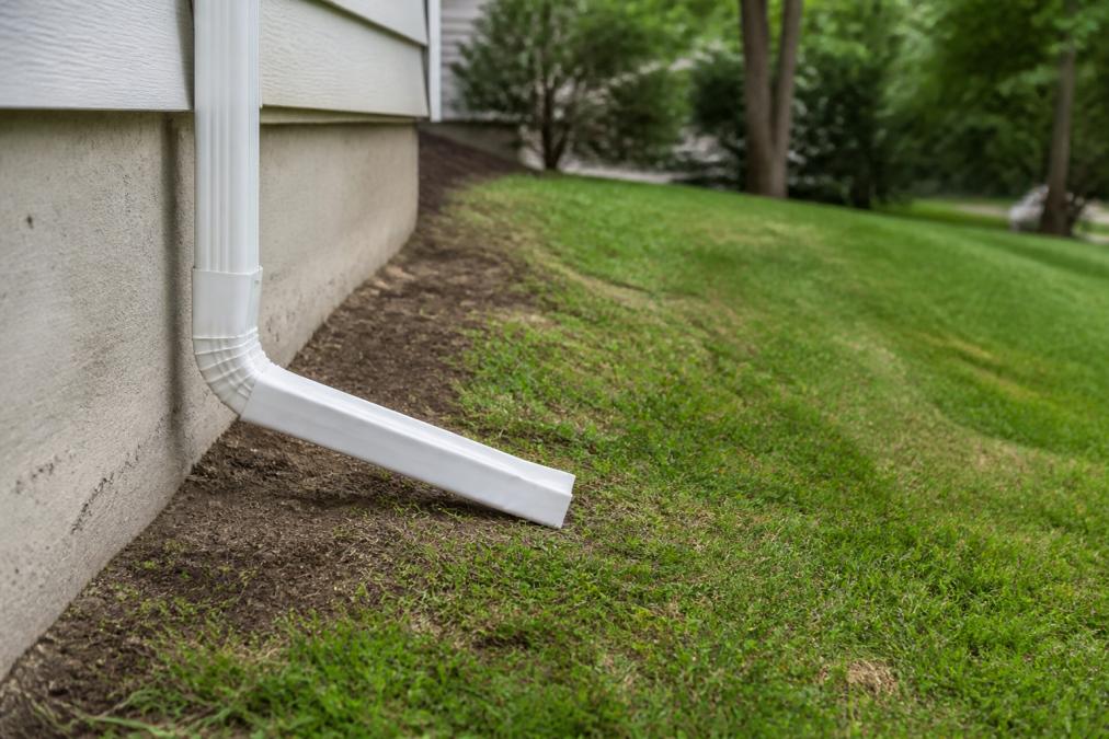 Close-up of a properly installed downspout extension directing water away from a home's foundation, with visible grading slope in the background