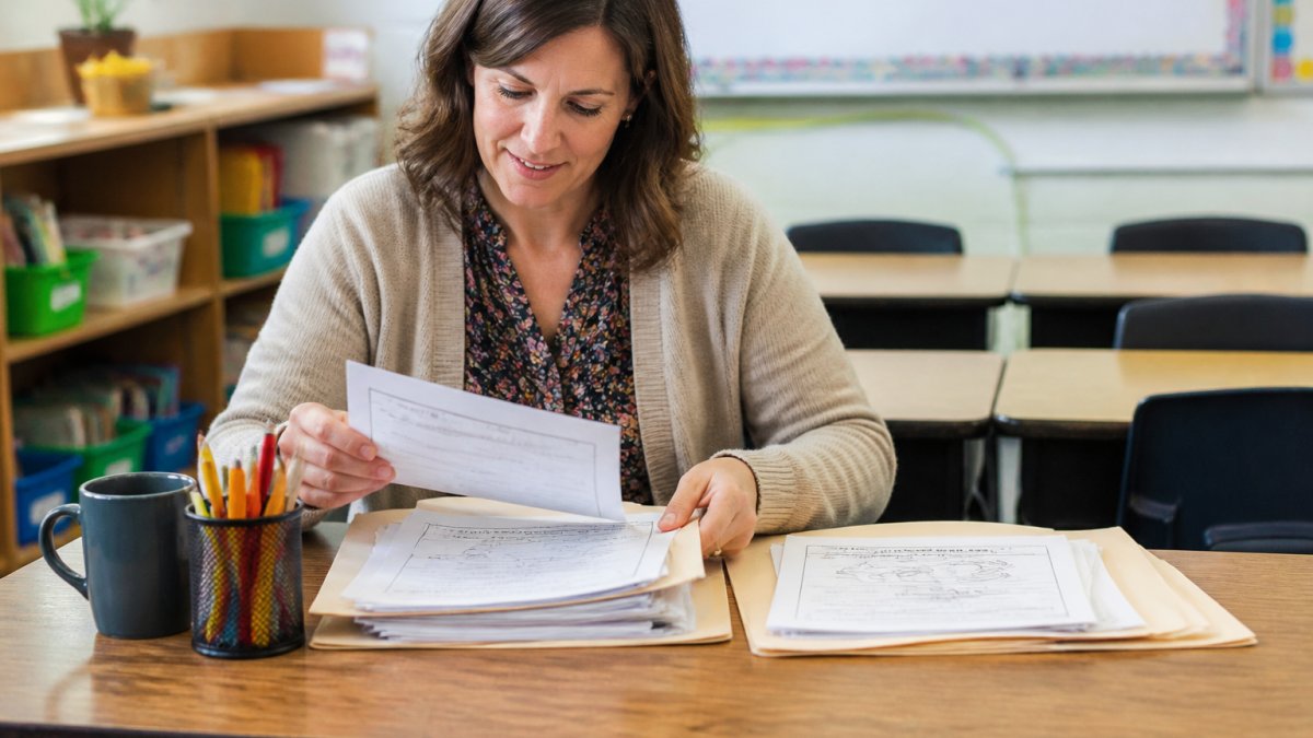 Elementary teacher organizing printable educational worksheets for teachers into folders at a bright desk.