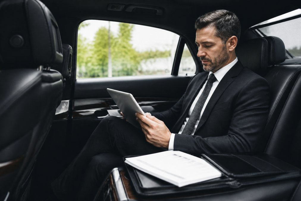 Business professional in modern office reviewing privacy documentation and security certifications on a tablet while seated in a luxury black vehicle interior, professional attire, natural lighting