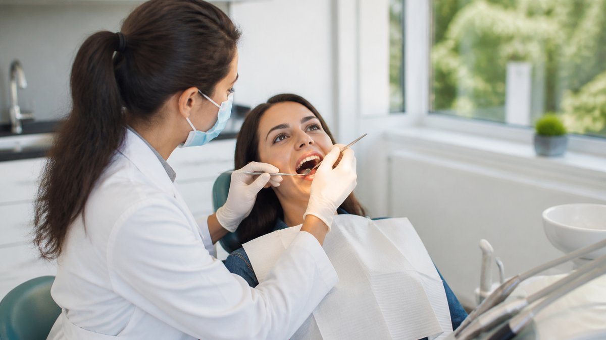 Dentist in white coat performing oral examination on patient in modern dental surgery with contemporary equipment and natural light