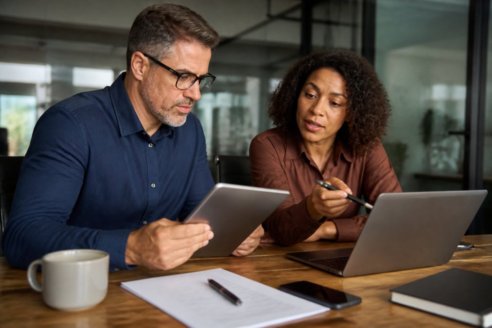 A team leader reviewing a security checklist on a tablet while a colleague points at a laptop screen showing access permissions in a modern office