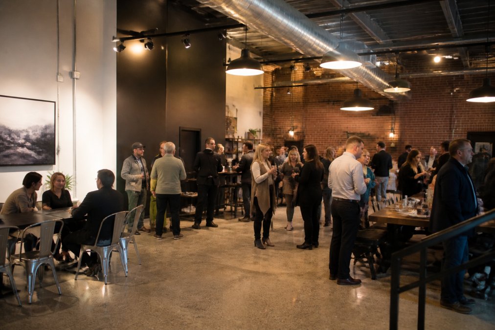 Modern coffee shop event space with flexible seating areas, industrial design elements, and groups of people gathered for a private event with warm overhead lighting