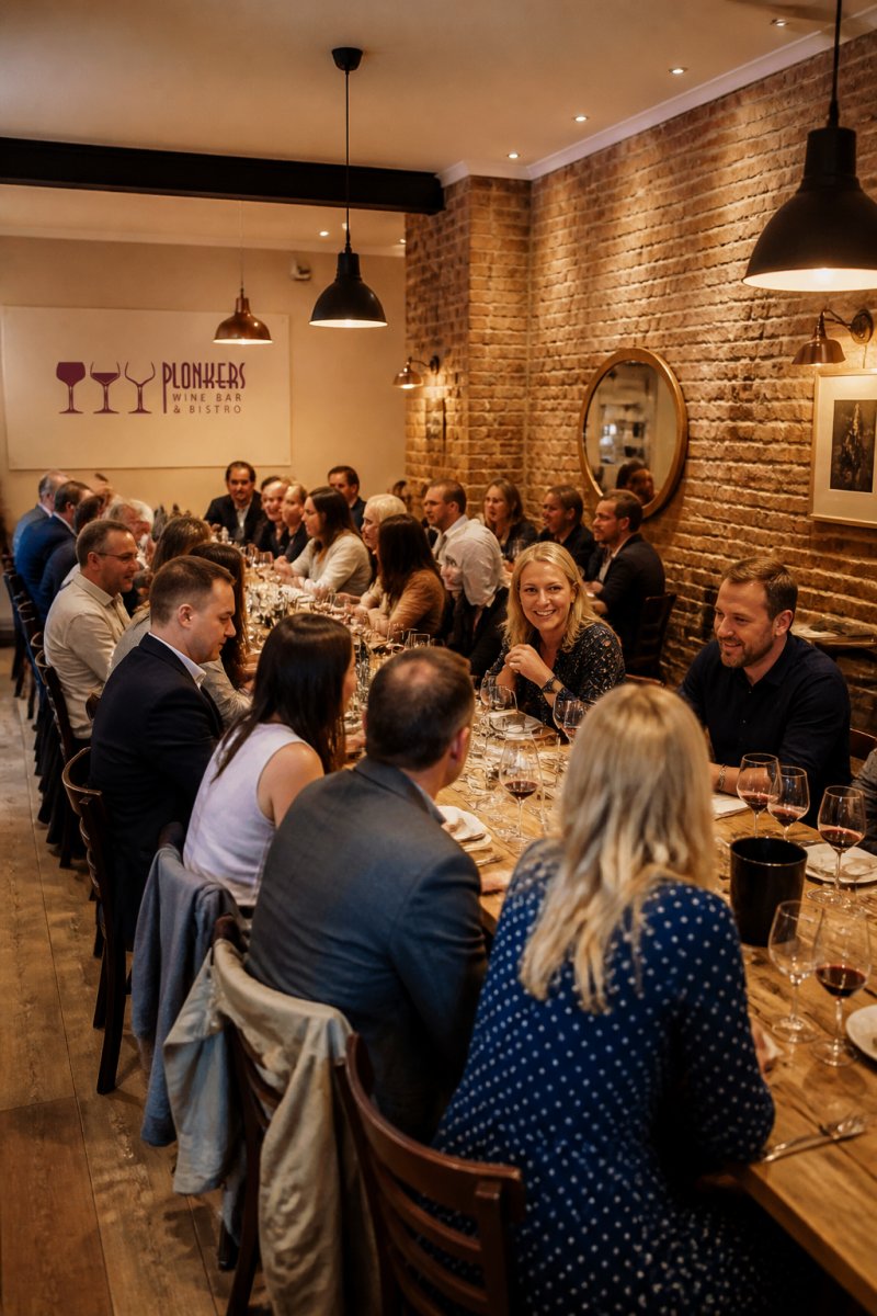 Forty guests seated at long wooden tables in a warm bistro with exposed brick walls, perfect for private event spaces.