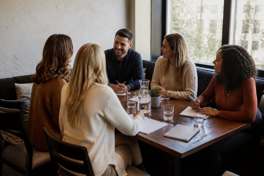 Team members collaborating in a cozy private dining or meeting room with comfortable seating, natural light, and visible amenities like water pitchers and notepads