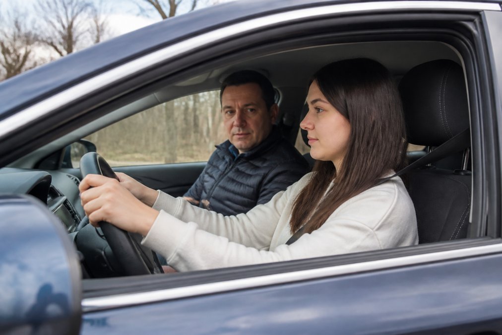 Driving instructor observing a focused student during private lessons vs group classes in a sedan.