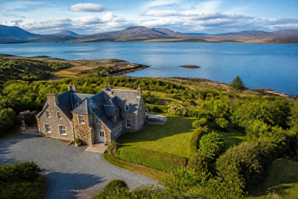 Aerial view of a luxury stone lodge nestled on the westerly coastline of Isle of Skye with manicured grounds, loch views, and mountains in the distance