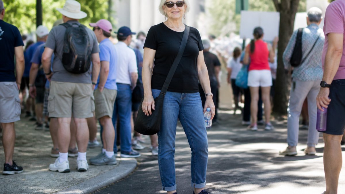 Woman over 50 wearing a pro-democracy message t-shirt with comfortable jeans and practical walking shoes, standing outdoors during daytime with confident posture and natural lighting