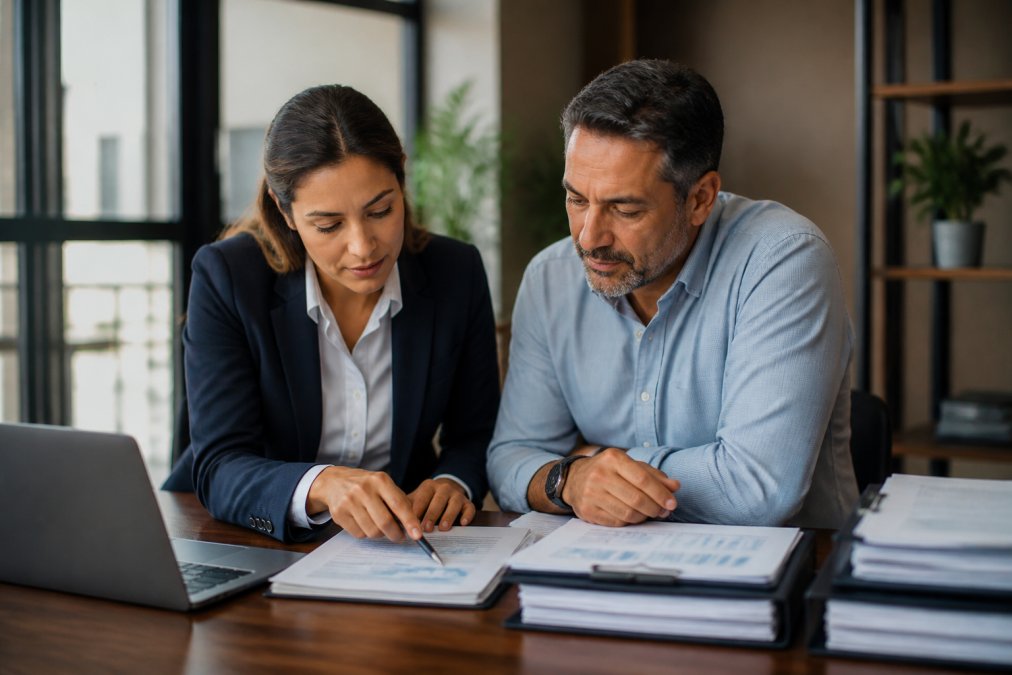 Tax professional and small business owner reviewing financial documents together at a clean desk with a laptop and organized folders, discussing tax strategy