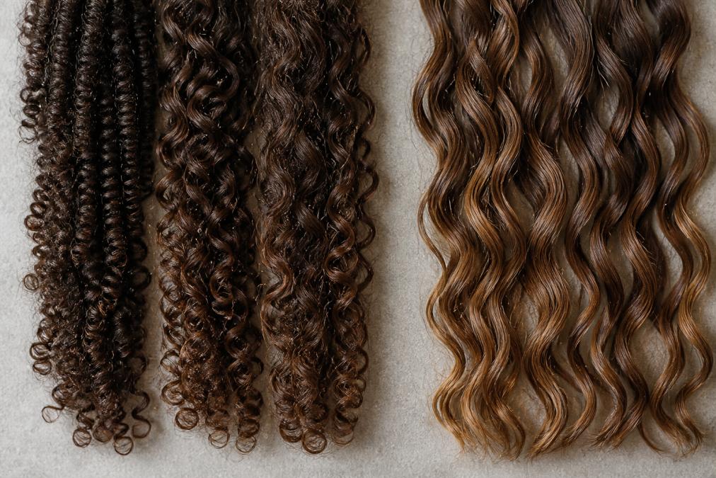 Close-up di diverse texture di capelli ricci: ricci stretti e definiti, ricci medi ondulati, capelli mossi leggeri, mostrando le variazioni naturali di forma e elasticità sotto illuminazione naturale